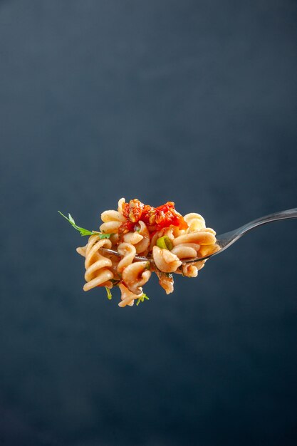 Rotini-Nudeln der Vorderansicht auf der Gabel auf freiem Raum der dunklen isolierten Oberfläche