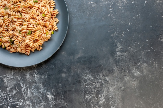 Rotini-Nudeln in der oberen Hälfte auf rundem Teller auf freiem Raum Lebensmittelfoto der dunklen Oberfläche