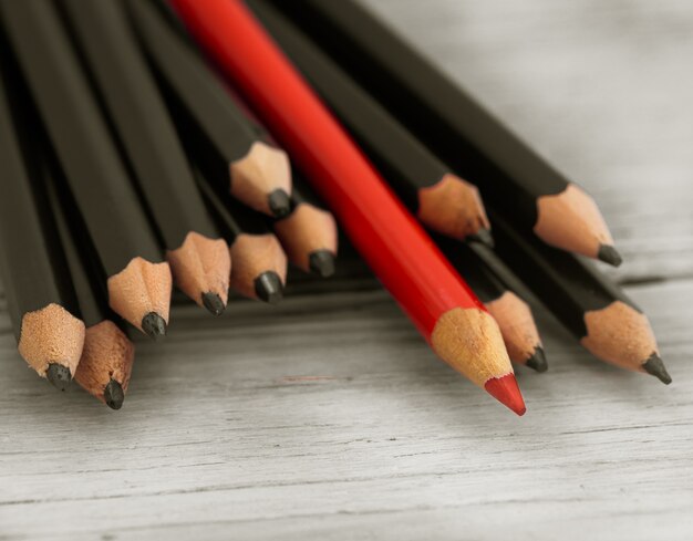 Rotstift hebt sich von der Menge des schwarzen Bleistifts auf einem hölzernen weißen Hintergrund ab.