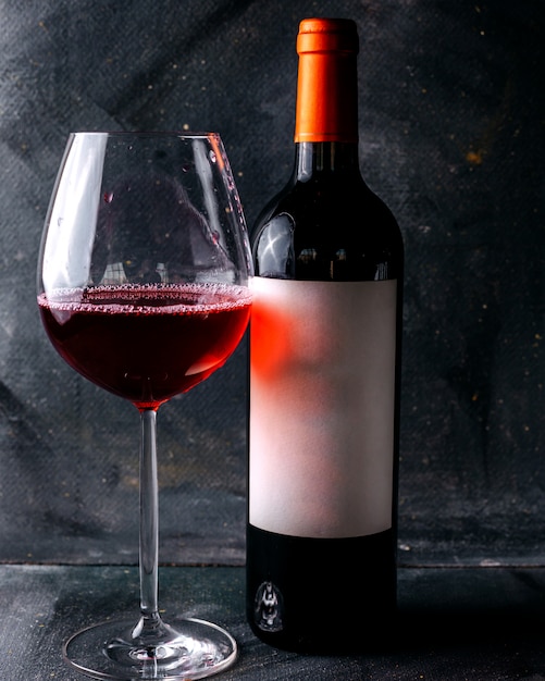 Rotwein der Vorderansicht zusammen mit Glas auf dem grauen Boden