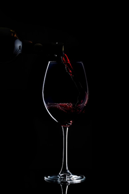 Rotwein wird im Dunkeln in Glas mit langem Stiel gegossen