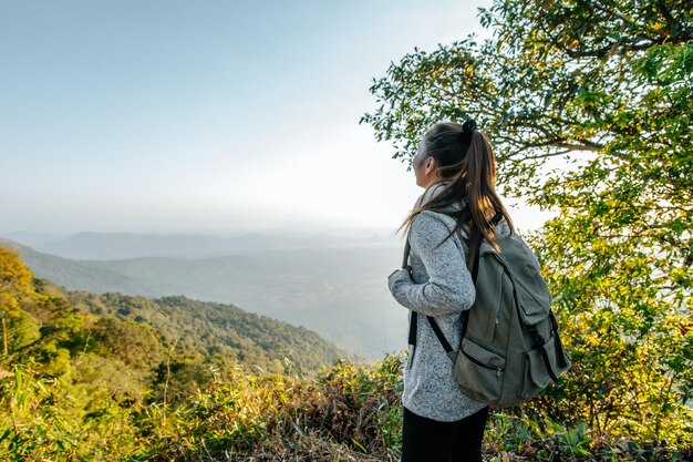 Rückansicht der jungen asiatischen Wanderfrau, die am Aussichtspunkt steht und eine schöne Aussicht mit glücklichem Blick auf den Gipfelberg und den Sonnenstrahl-Kopienraum hat