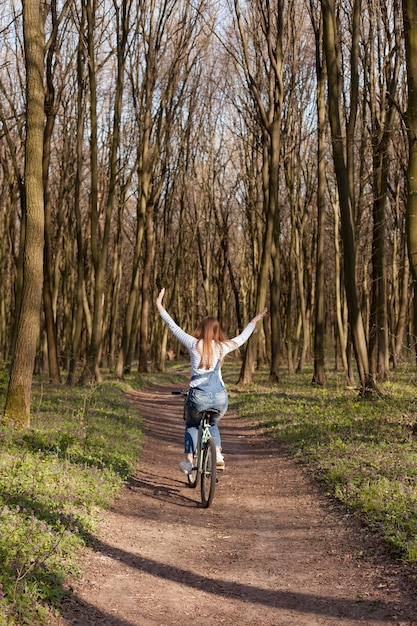 Kostenloses Foto rückansicht der sorglosen frau, die fahrrad im wald reitet