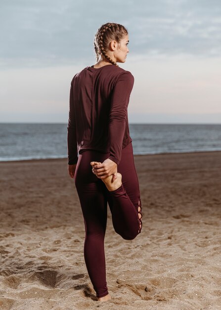 Rückansicht der sportlichen Frau, die durch den Strand streckt