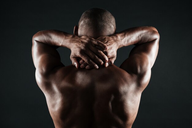 Rückansicht des jungen afrikanischen Mannes mit dem muskulösen Körper, der seinen Hals hält