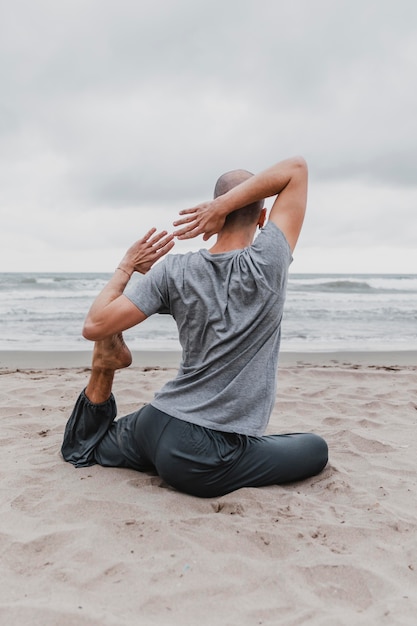 Rückansicht des Mannes am Strand, der Yoga ausübt