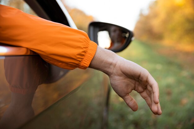 Rückansicht des Mannes, der seine Hand während einer Straßenfahrt aus dem Auto holt