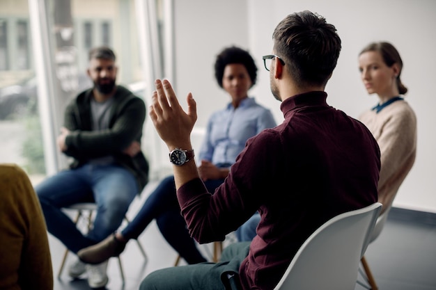 Rückansicht des Mannes mit erhobener Hand bei Gruppentherapie im medizinischen Zentrum