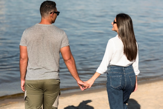 Rückansicht des romantischen Paares, das Hände am Strand hält