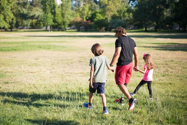 Rückansicht des Vaters mit Behinderung, der mit Kindern geht. Mann mit mechanischem Bein, das mit Jungen und Mädchen im Park spazieren geht. Behinderung, Familie, Liebeskonzept