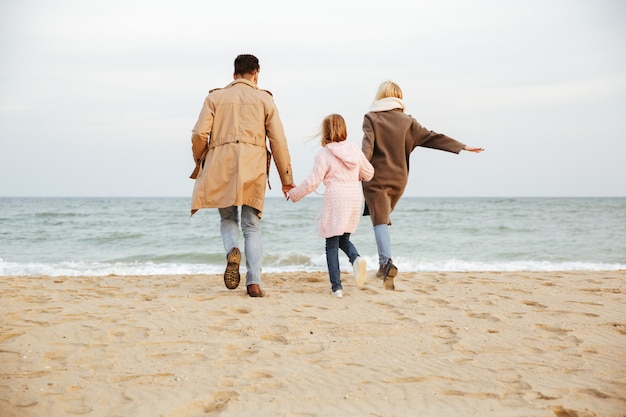 Rückansicht einer jungen Familie mit einer kleinen Tochter, die Spaß am Strand zusammen hat und läuft