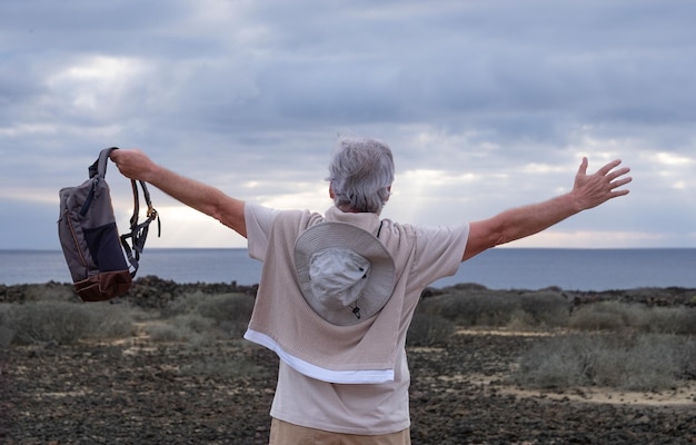 Rückansicht eines älteren grauhaarigen mannes mit offenen armen bei einem ausflug im freien mit blick auf meer und horizont