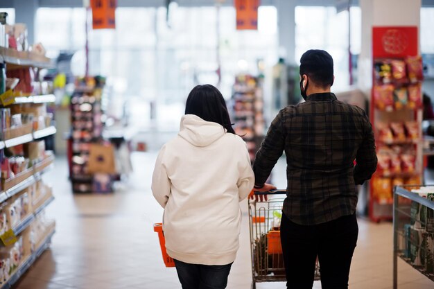 Rückansicht eines asiatischen Paares, das während einer Pandemie eine schützende Gesichtsmaske beim gemeinsamen Einkaufen im Supermarkt trägt