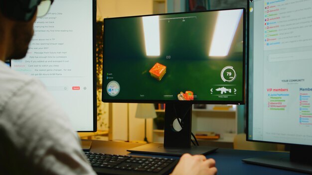 Rückansicht eines jungen Mannes, der kompetitive Shooter-Spiele auf dem Computer mit zwei geöffneten Streaming-Chats spielt