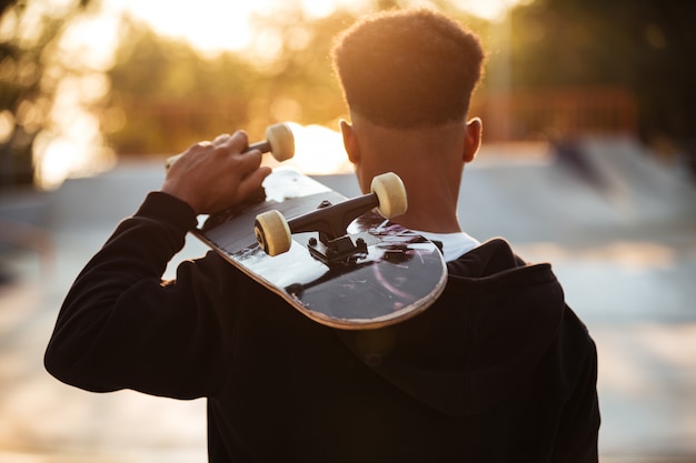 Rückansicht eines männlichen Teenager-Mannes, der Skateboard hält