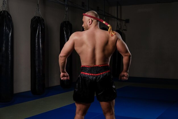 Rückansicht eines Muay-Thai-Kämpfers mit einem muskulösen Körper in traditioneller Uniform im Fitnessstudio