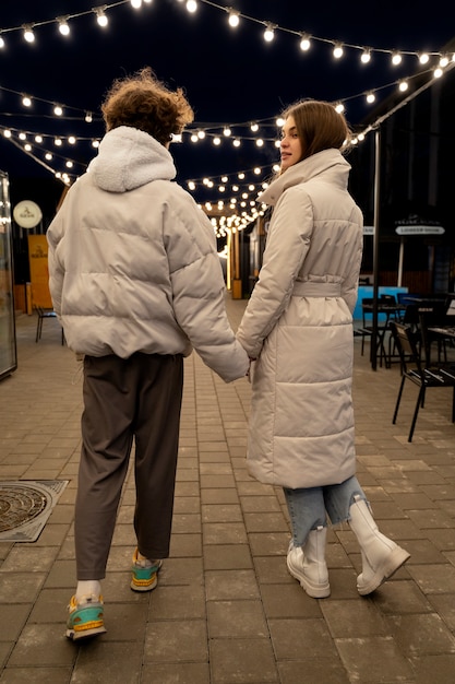 Kostenloses Foto rückansicht eines paares, das sich draußen bei lichtern händchen hält