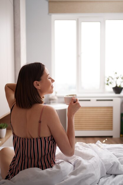 Rückansicht Frauen, die Kaffee auf dem Bett genießen, während sie sich nach dem Aufwachen strecken.