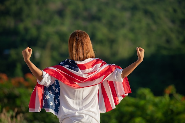 Rückansicht glückliche junge Frau, die mit der USA-Nationalflagge im Freien bei Sonnenuntergang posiert.