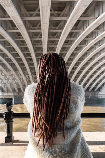 Kostenloses Foto rückansicht von afro-dreadlocks auf einer frau, die im freien unter einer brücke posiert