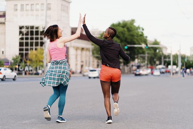 Rückansicht von Freunden in Sportkleidung, die in der Stadt laufen und multiethnische Frauen bei einem Fitnesstraining diskutieren