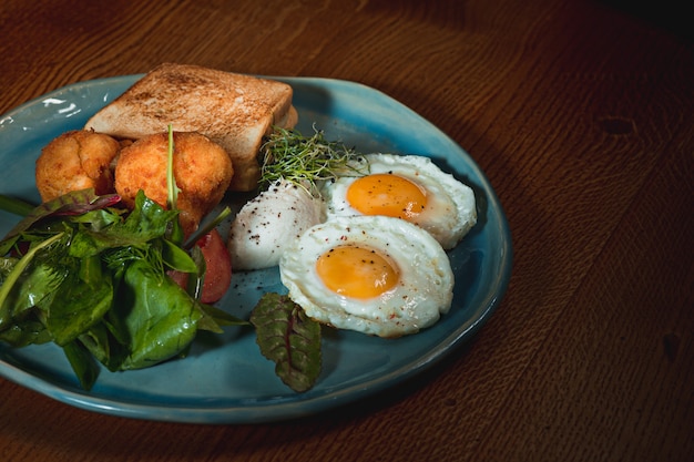 Rührei auf Fleisch mit Bratkartoffeln und Toast auf Teller auf Holztisch