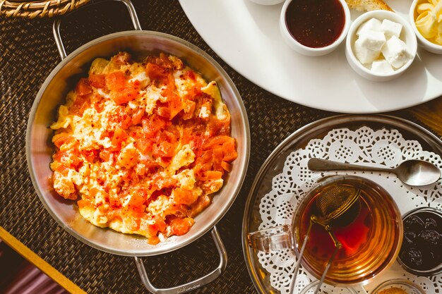 Rührei von oben mit Tomaten in einer Pfanne und einer Tasse Tee mit Marmelade