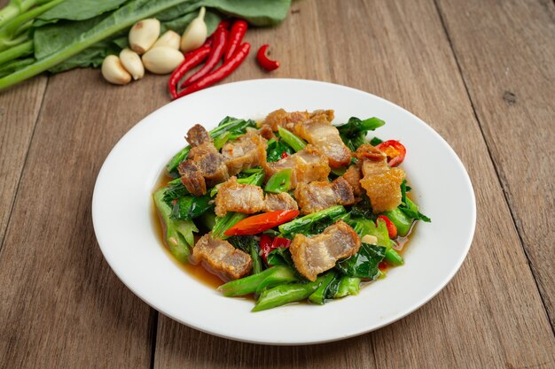 Rühren Sie gebratenen Grünkohl, würziges knuspriges Schweinefleisch auf thailändischem Lebensmittelkonzept des Holztischs.