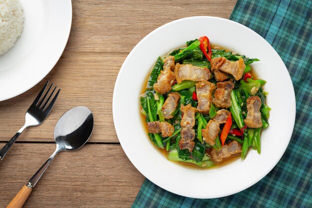 Rühren Sie gebratenen Grünkohl, würziges knuspriges Schweinefleisch auf thailändischem Lebensmittelkonzept des Holztischs.