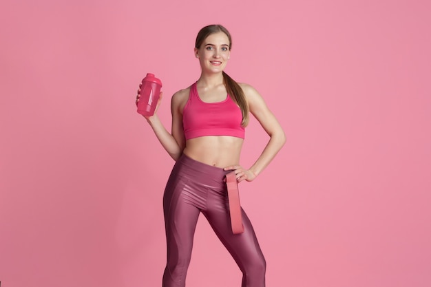 Kostenloses Foto ruhen. schöne junge sportlerin üben, einfarbiges rosa porträt. kaukasisches modell der sportlichen passform mit trinkflasche. bodybuilding, gesunder lebensstil, schönheits- und aktionskonzept.