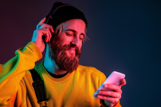 Ruhig, glücklich, telefonisch. porträt des kaukasischen mannes auf gradientenraum im neonlicht