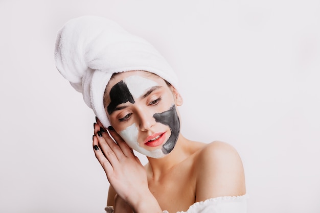 Ruhige Dame in Tonmaske für Gesicht posiert auf weißer Wand. Porträt der Frau, die Abendhygiene tut.