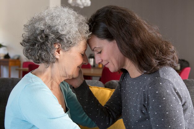 Ruhige erwachsene Tochter und ältere Mutter, die auf Sofa sitzt