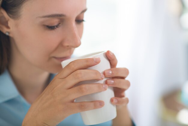 Ruhige junge hübsche Frau, die Schale hält und Kaffee trinkt