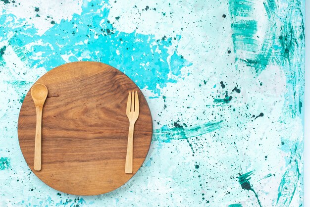 Rundansicht runder hölzerner Schreibtisch braun gefärbt mit Holzlöffelgabel auf dem hellblauen Hintergrundfoto Farbküchenlebensmittel