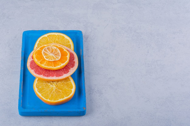 Runde Scheiben frischer Grapefruit, Orange und Zitrone auf blauem Teller.