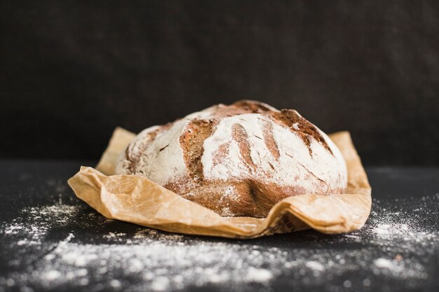 Rundes frisch gebackenes rundes Brot des rustikalen Roggens auf braunem Papier gegen schwarzen Hintergrund