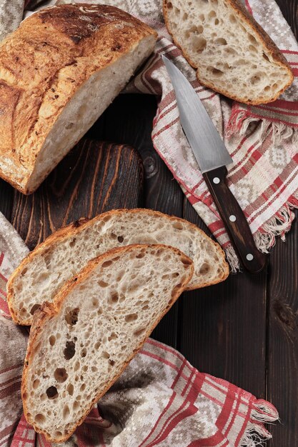 Rundes rustikales Brot ohne Kneten in Stücke geschnitten auf einem Schneidebrett auf einem alten dunklen rustikalen Tisch Hausgemachtes Vollkornbrot-Layout auf dem vertikalen Tischrahmen