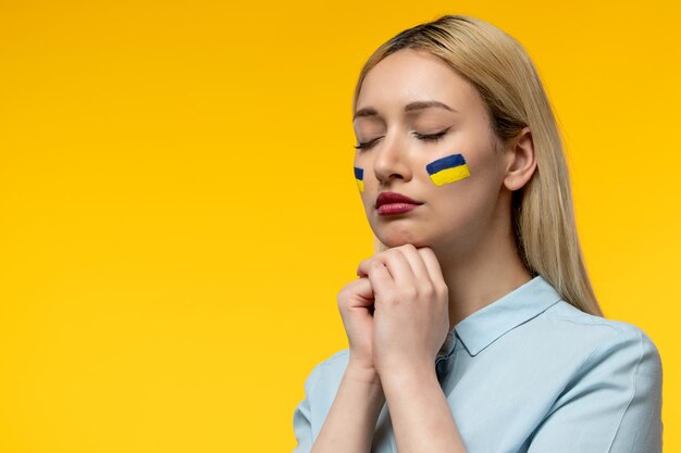 Russisch-ukrainischer Konflikt junges süßes Mädchen mit ukrainischer Flagge auf den Wangen, die geschlossene Augen betet