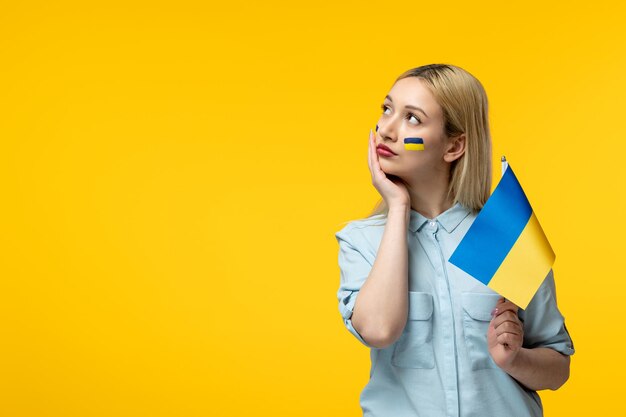 Russisch-ukrainischer Konflikt junges süßes Mädchen mit ukrainischer Flagge auf den Wangen, die mit Flagge nach oben schauen