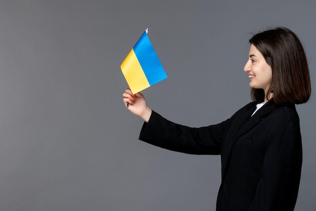 Kostenloses Foto russischer konflikt in der ukraine süße junge frau mit dunklen haaren im schwarzen blazer lächelnd auf die flagge schauend