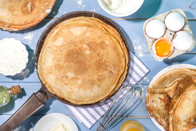 Russischer ukrainischer europäischer feiertag maslenitsa. traditionelle dünne crêpes-pfannkuchen, auf blauem holztisch mit zutaten zum kochen - mehl, eier, butter, kopienraum von oben Premium Fotos