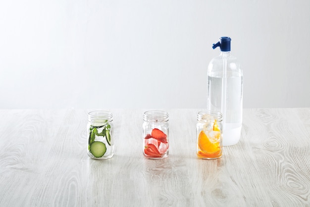 Rustikale Gläser mit Eis und verschiedenen Füllungen. Orange, Erdbeere, Gurke und Minze zubereitet, um frische hausgemachte Limonade mit Sprudelwasser von Syphone zu machen.