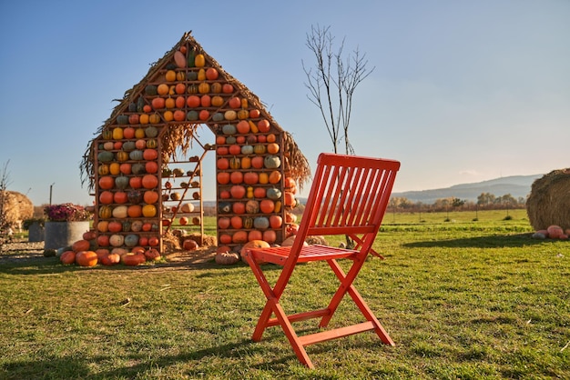 Rustikaler Stuhl und künstliches Kürbishaus in grünem Rasen im November mit niedrigem Blickwinkel
