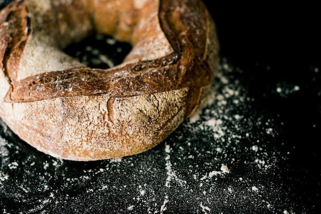 Rustikales rundes Brot wischte mit Mehl auf schwarzem Hintergrund ab