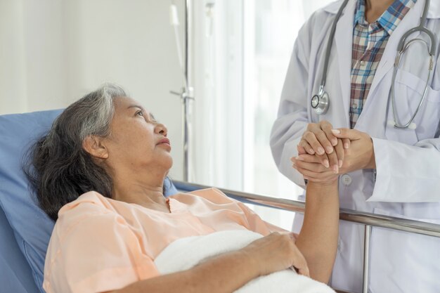 Ärzte halten Hände, um ältere ältere Patientinnen im Krankenhaus-Senioren-Frauen-Medizin- und Gesundheitskonzept zu ermutigen