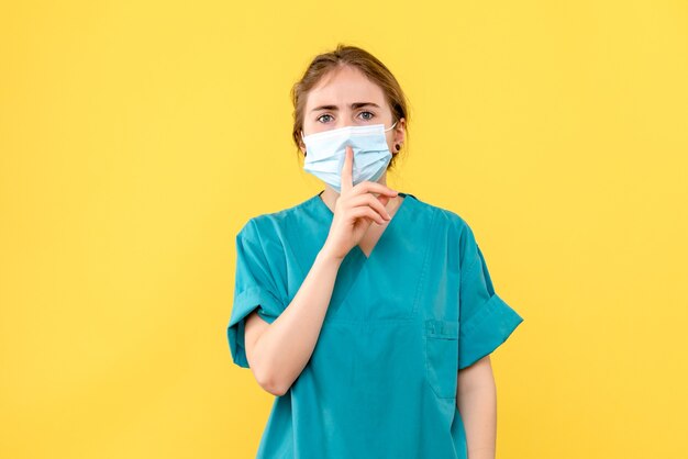 Ärztin der Vorderansicht, die bittet, Schweigen auf Krankenhauspandemie des gelben Hintergrundkrankenhauses zu halten