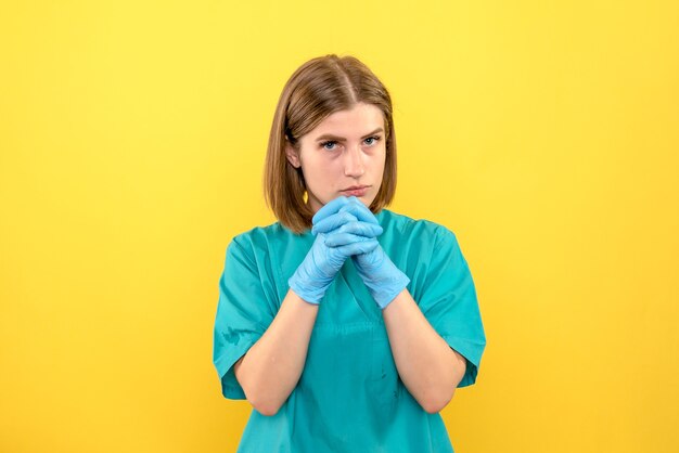 Ärztin der Vorderansicht, die blaue Handschuhe auf gelbem Raum trägt