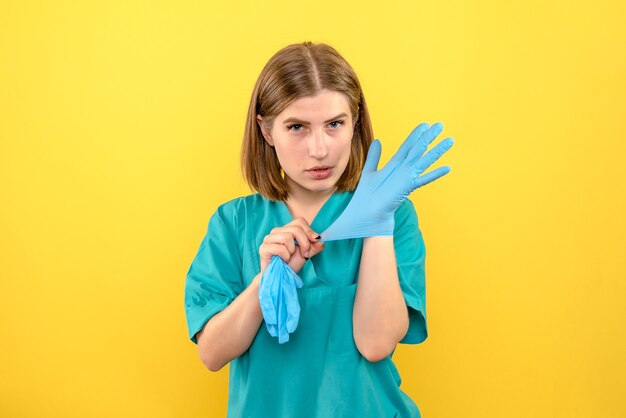 Ärztin der Vorderansicht, die blaue Handschuhe auf gelbem Raum trägt