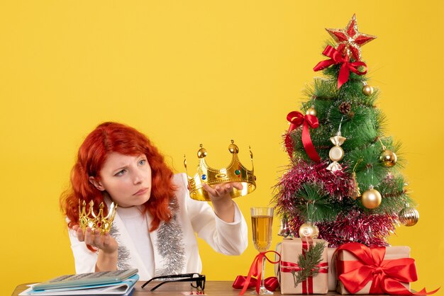 Ärztin der Vorderansicht, die Kronen um Weihnachtsbaum und Geschenke hält